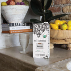 Milkadamia carton beside glass to show size and pourable consistency
