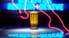 Monster Rehab can beside a smartphone showing 15.5 oz scale for size and portability
