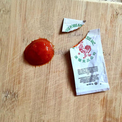 Sriracha2Go packet beside coin showing compact TSA-friendly size