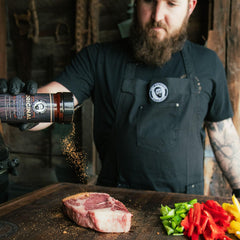 Bearded Butcher Black shaker next to grilled steak crust highlighting bold peppery sear benefit