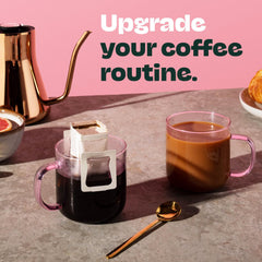 Single Copper Cow Coffee decaf pour-over packet beside a disposable filter, convenient single-serve visual