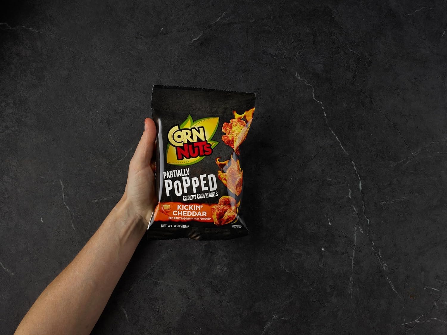 Hand holding a 3 oz Corn Nuts Kickin’ Cheddar bag showing pocket-sized convenience