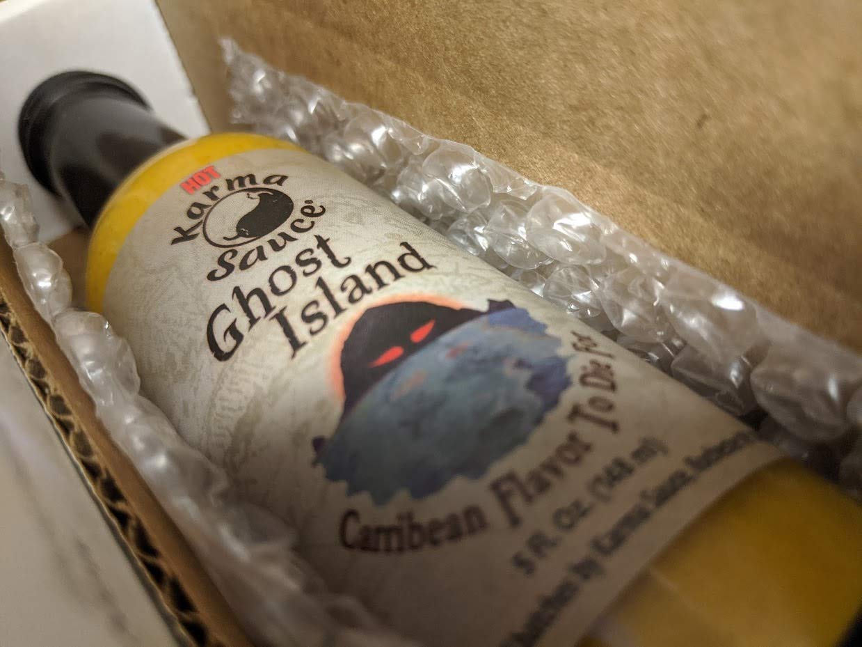 Karma Sauce Ghost Island bottle on table with mango and pineapple, suggests Caribbean-inspired flavor