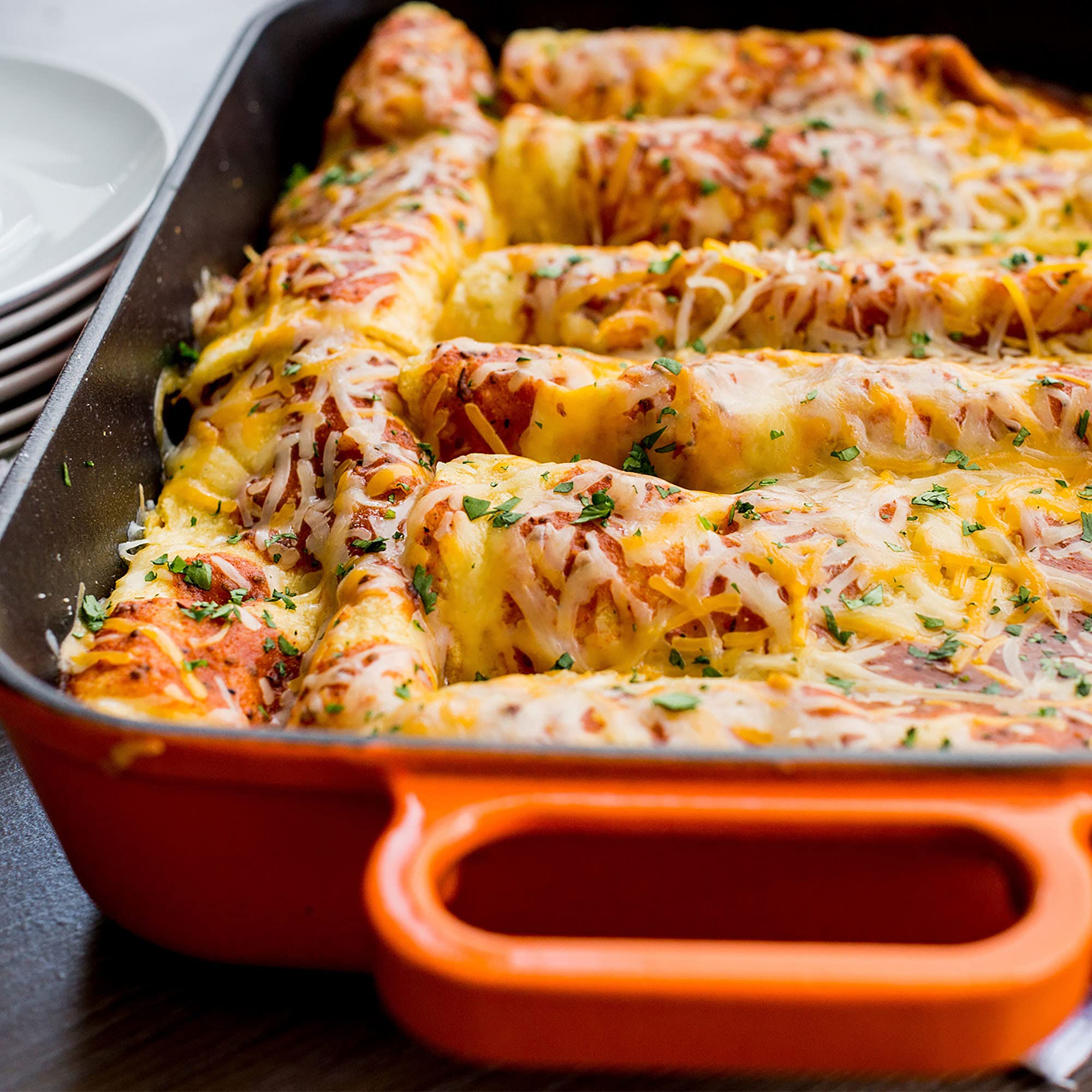 Sauce made from McCormick mix being poured into baking pan, ensures evenly seasoned enchiladas