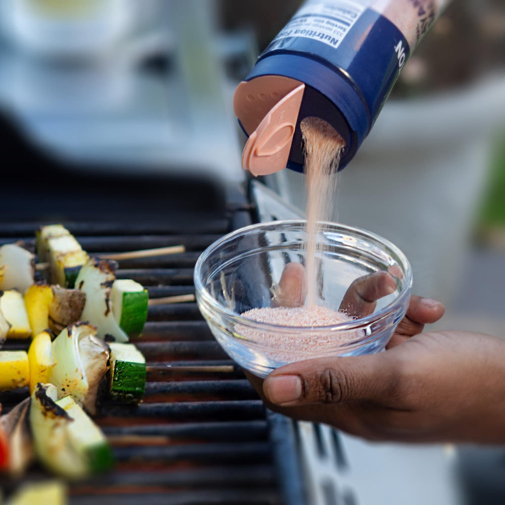 Morton pink salt pouring from container onto food showing easy seasoning benefit