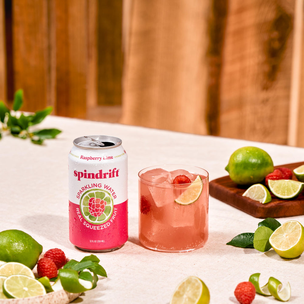 Fresh raspberries and lime next to Spindrift can showcasing real fruit ingredients benefit